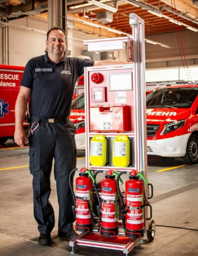 Ein Feuerwehrmann steht neben einem dem Fire Point Trolley – ein mobiler Brandschutzcontainer zur temporären Brandüberwachung auf Baustellen oder bei Veranstaltungen